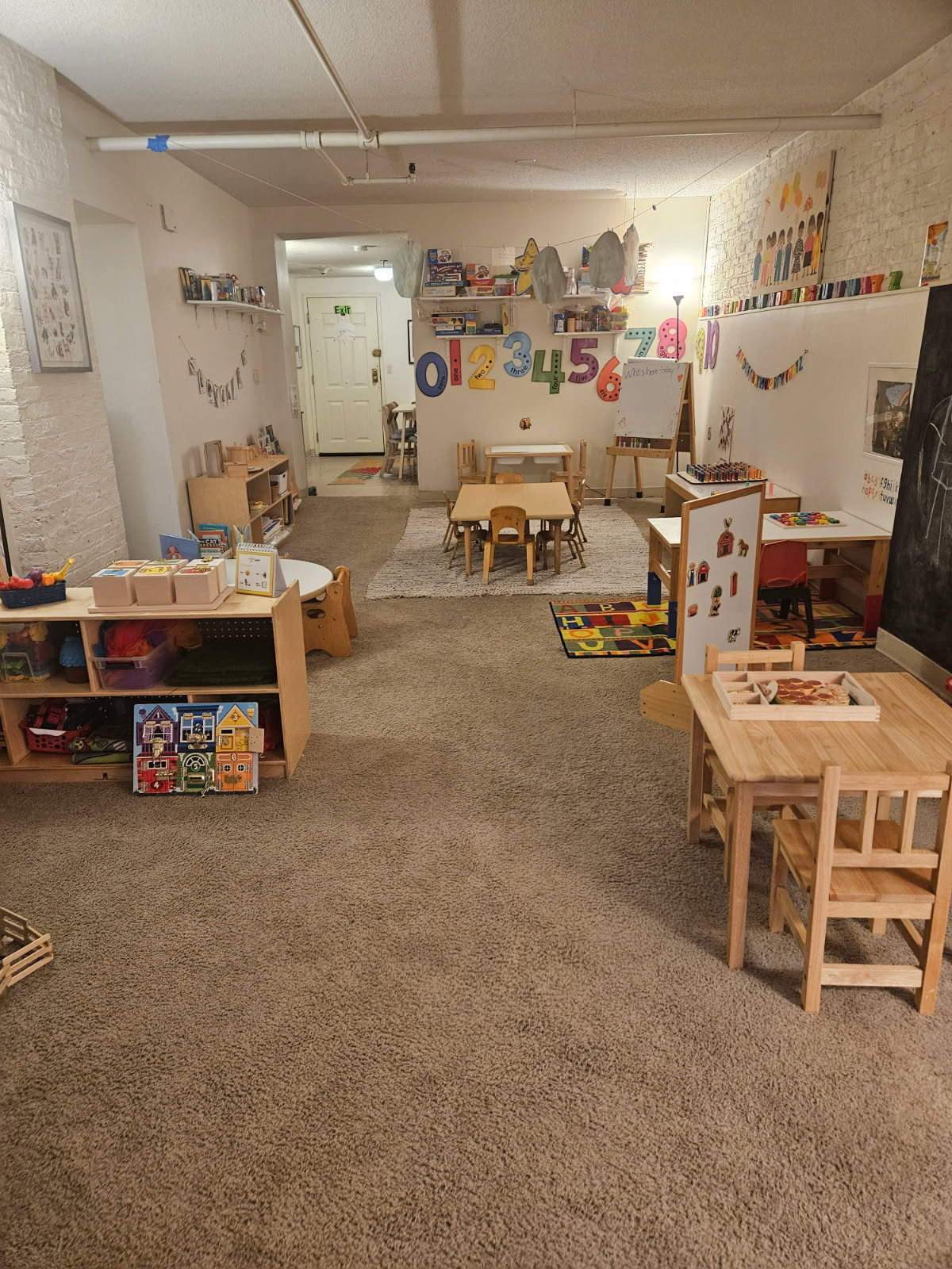 The full space end to end: a number wall, a painting easel, low work tables and chairs, and open shelving along the walls.